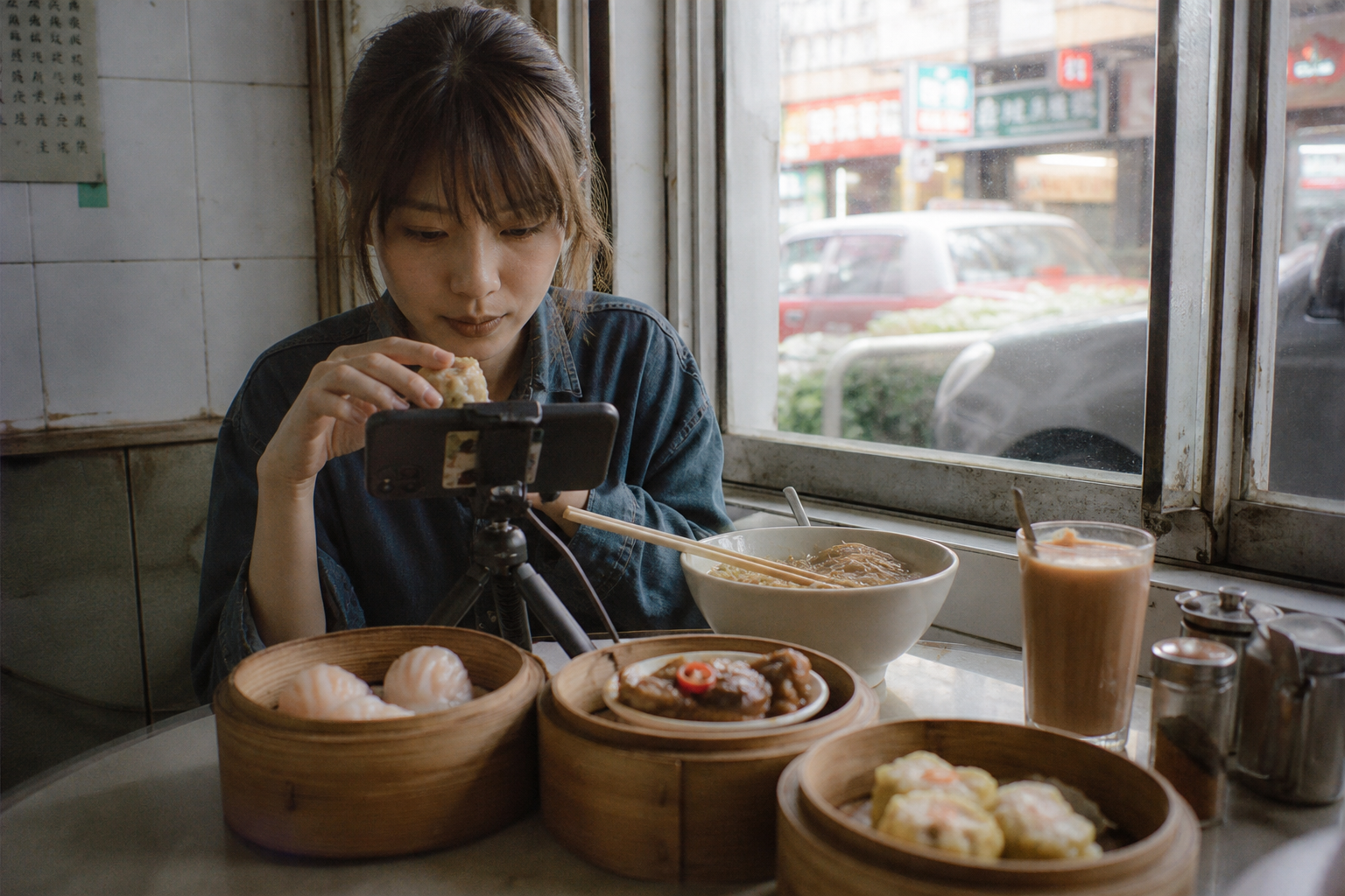 茶餐廳枱面特寫：蒸籠、奶茶與手機支架，創作者準備拍探店短片